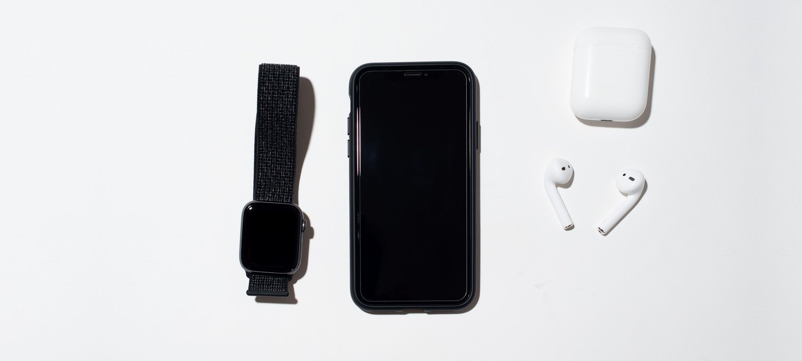 Smartphone, smartwatch and wireless earbuds laid out on a white desk